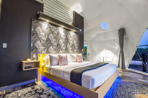 Modern bedroom with a stylish bed, patterned wall, and unique dome-shaped ceiling, featuring ambient lighting.