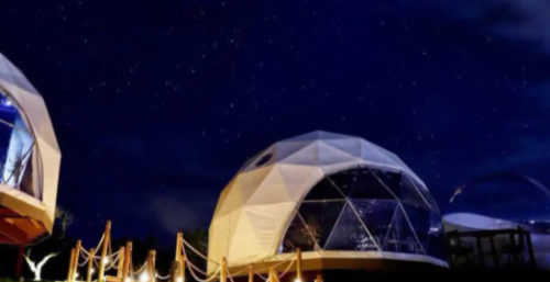 Two geodesic domes under a starry night sky, surrounded by a wooden railing and lush greenery.