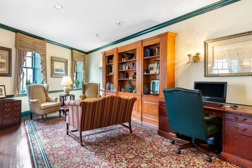 Cozy office with a wooden bookshelf, two armchairs, a desk with a computer, and decorative wall art.