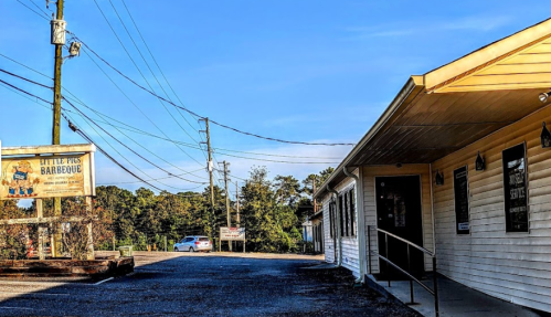 A barbecue restaurant with a sign, surrounded by power lines and trees under a clear blue sky.