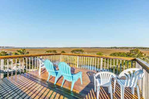 A deck with white chairs overlooks a scenic view of a marsh and clear blue sky.