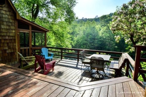 A wooden deck with colorful chairs overlooks a lush green landscape and trees in the background.