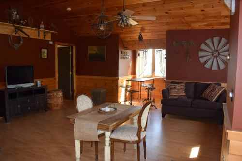 Cozy living space with wooden walls, a sofa, dining table, and a TV, featuring rustic decor and natural light.