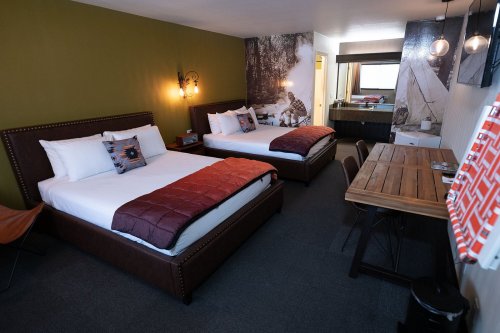 A cozy hotel room featuring two beds, a wooden table, and a modern design with nature-themed decor.