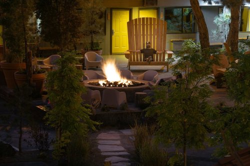 A cozy outdoor fire pit surrounded by seating, with a large wooden chair and a softly lit building in the background.