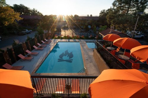 A pool with orange umbrellas and lounge chairs, reflecting a sunset and a campfire design on the water's surface.