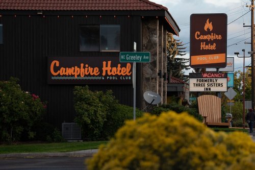 Signage for Campfire Hotel & Pool Club, with a nearby street sign and a flower bush in the foreground.