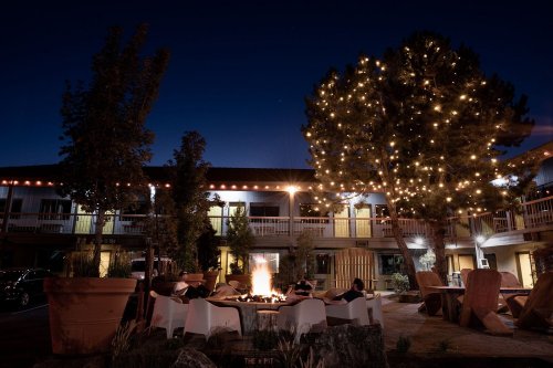 Cozy outdoor seating area with a fire pit, surrounded by trees adorned with lights, at dusk.