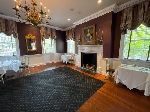 Elegant dining room with a chandelier, fireplace, and white tablecloths, featuring rich purple walls and large windows.