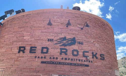 Sign for Red Rocks Park and Amphitheatre, featuring a stone wall and blue sky with clouds. Established 1941.