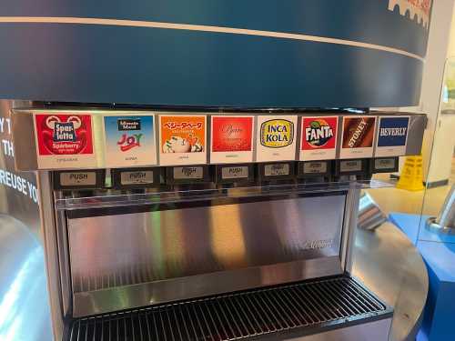 A soda fountain with various drink options, including Sprite, Fanta, and Inca Kola, displayed on a blue machine.