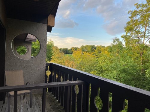 A balcony view overlooking lush green trees and a clear sky, with a circular window in the wall.