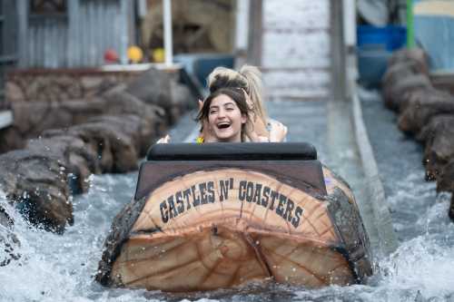 A group of friends joyfully rides a log flume, splashing through water at an amusement park.