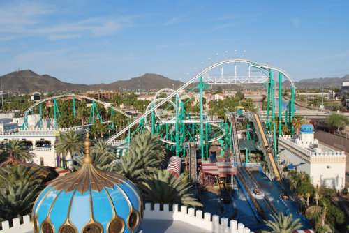 Aerial view of a vibrant amusement park featuring roller coasters, water rides, and palm trees under a clear blue sky.