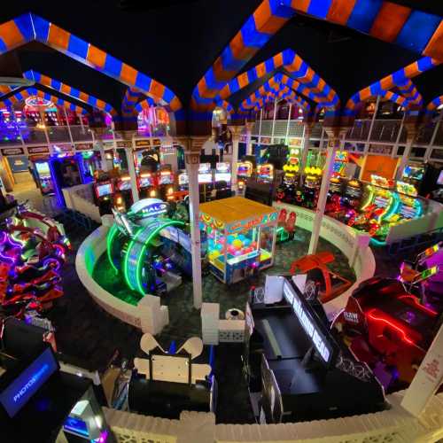 A vibrant arcade filled with colorful lights, games, and attractions, featuring various gaming stations and rides.