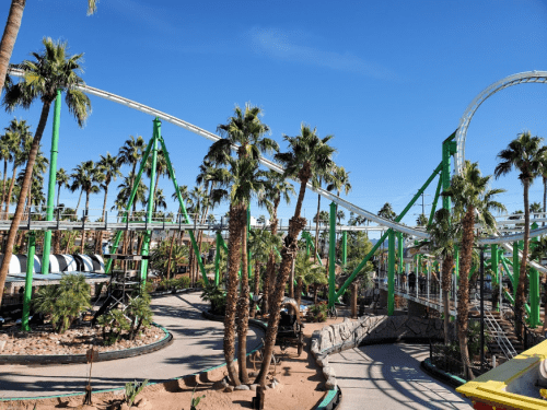 A roller coaster with green supports surrounded by palm trees under a clear blue sky.