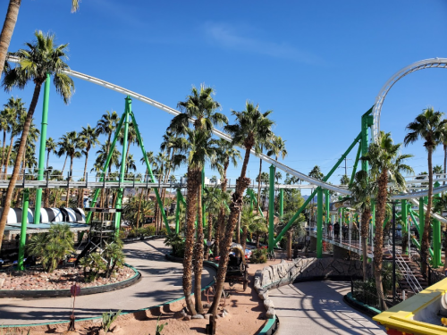 A roller coaster with green supports surrounded by palm trees under a clear blue sky.
