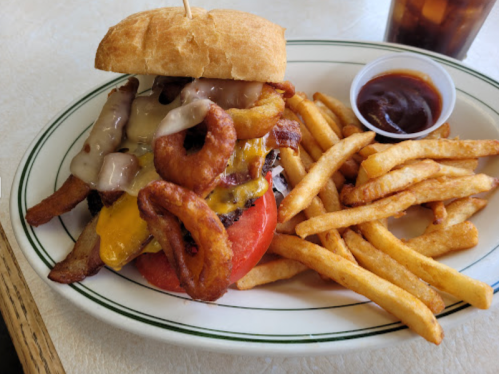A hearty burger topped with cheese, onion rings, and tomato, served with fries and a side of barbecue sauce.
