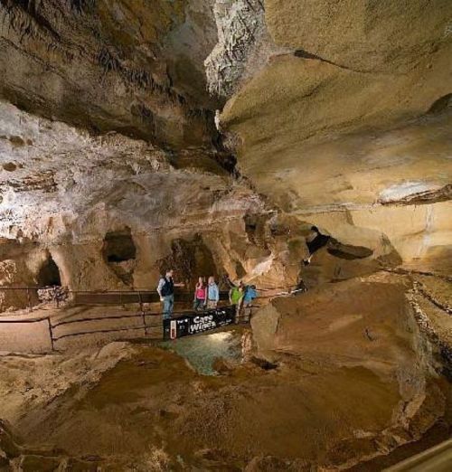 A group of visitors explores a large cave with rock formations and a railing for safety.