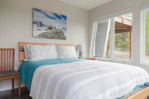 Cozy bedroom featuring a bed with a blue and white blanket, a chair, and large windows with a scenic view.