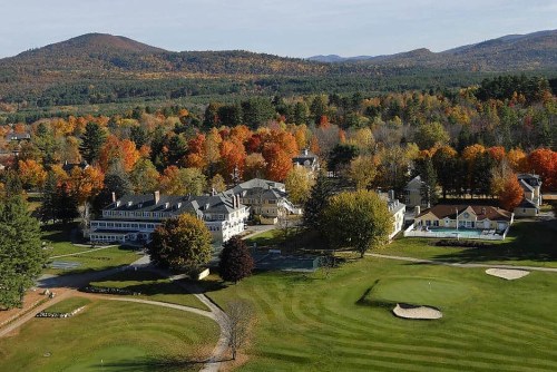 Aerial view of a resort surrounded by colorful autumn trees and rolling hills, with a golf course in the foreground.