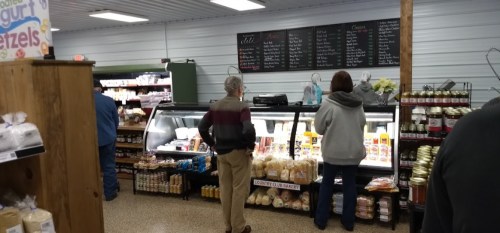 A grocery store interior with customers browsing refrigerated displays and shelves filled with various products.