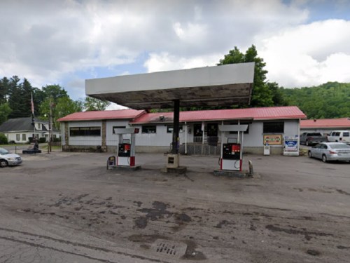 A gas station with two pumps and a building, surrounded by trees and cloudy skies.