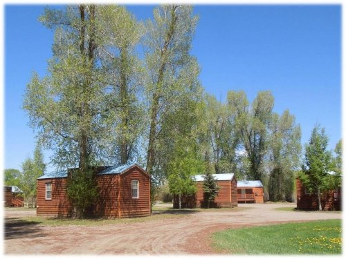 A scenic view of rustic cabins surrounded by tall trees and a clear blue sky.