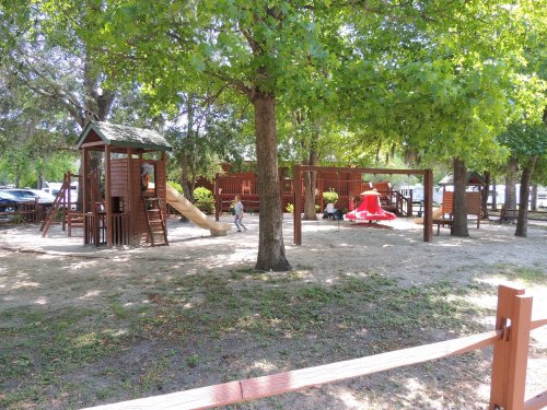 A playground with slides and climbing structures surrounded by trees and grassy areas, with a child playing.