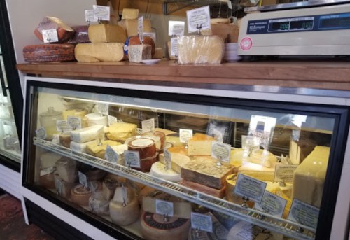 A display case filled with various types of cheese, each labeled with names and prices, set in a cheese shop.