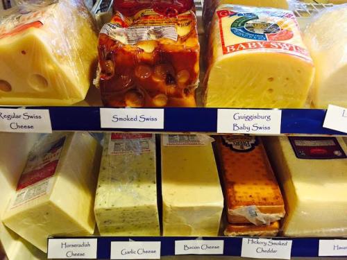 A variety of cheeses displayed on shelves, including Swiss, smoked, garlic, and cheddar varieties, with labels.