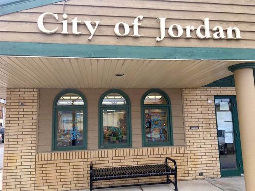 Sign for "City of Jordan" on a building with arched windows and a bench in front.