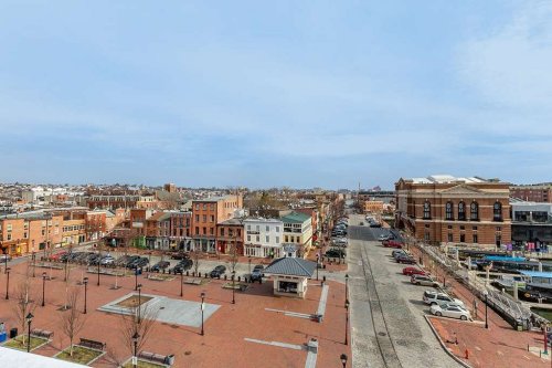 A wide view of a city street with brick buildings, parked cars, and a clear blue sky in the background.