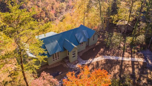 Aerial view of a green house with a blue roof surrounded by autumn trees and a stone pathway.