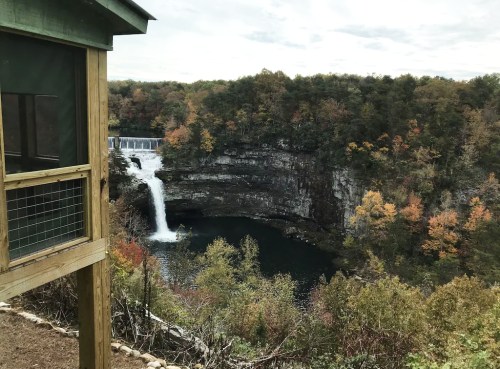 A scenic view of a waterfall cascading into a pool, surrounded by autumn foliage and rocky cliffs.