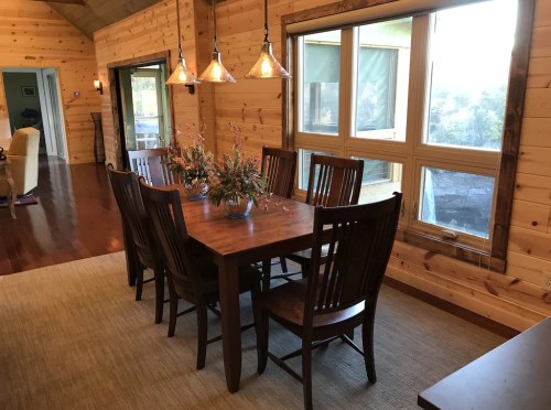 A wooden dining table with chairs, surrounded by a cozy, rustic interior and large windows letting in natural light.