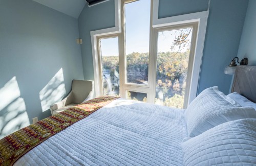 Cozy bedroom with a large window overlooking a scenic view of trees and water, featuring a neatly made bed.