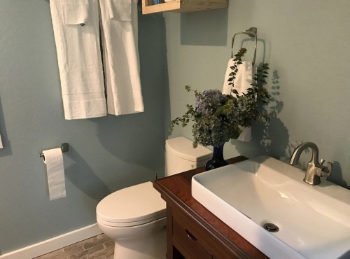 A modern bathroom featuring a wooden vanity, white sink, toilet, and a vase of flowers on the counter.
