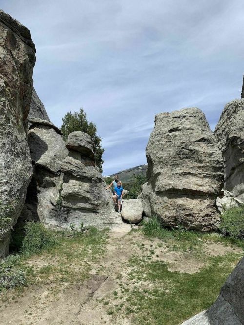 A person in a blue shirt stands between large rock formations in a natural landscape under a cloudy sky.