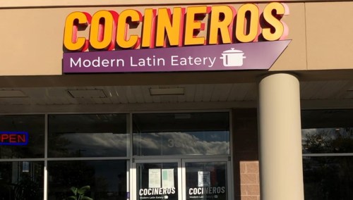 Sign for "Cocineros Modern Latin Eatery" on a restaurant exterior, with an "Open" sign in the window.