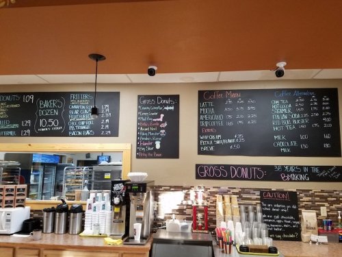 Chalkboard menu displaying prices for donuts, coffee, and bakery items in a cozy cafe setting.