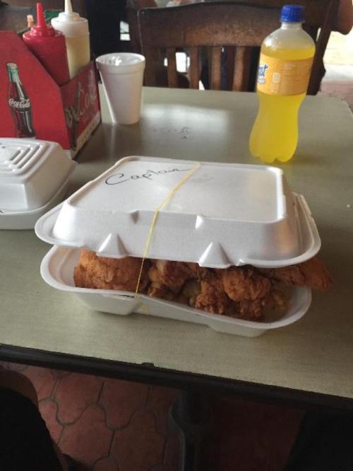 A stack of two takeout containers filled with fried chicken, sitting on a table with a drink and condiments nearby.