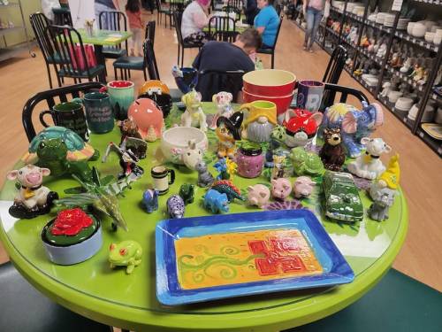 A colorful display of various ceramic figurines and pottery on a green table in a craft studio.