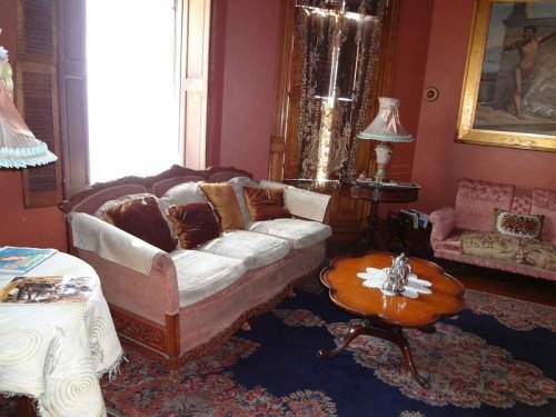 A vintage living room with ornate furniture, a wooden coffee table, and decorative lamps against a warm-colored wall.
