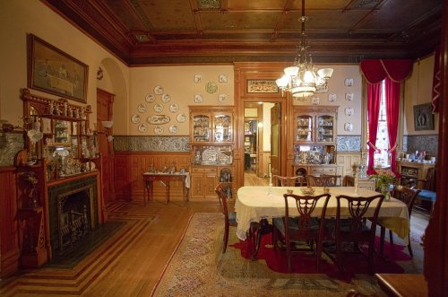 A vintage dining room with a wooden table, chairs, decorative plates on the walls, and elegant furnishings.
