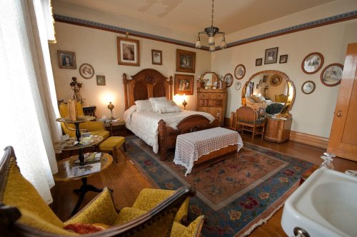 A vintage bedroom with a wooden bed, antique furniture, framed photos on the walls, and a cozy atmosphere.