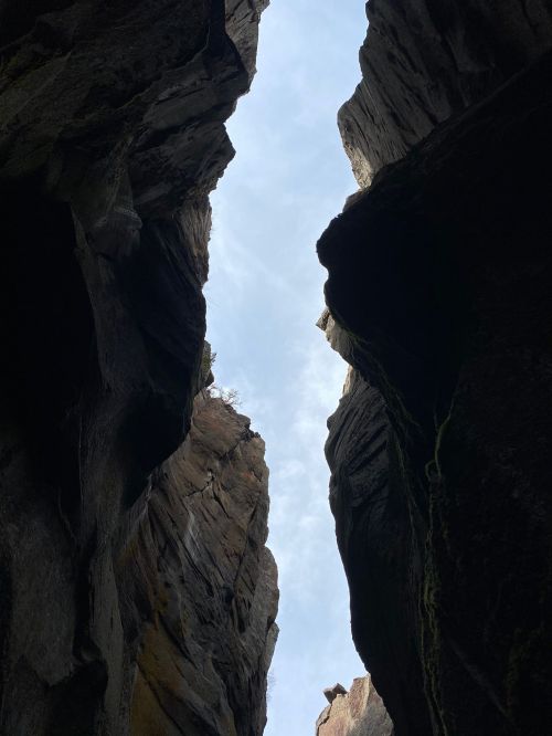 A narrow canyon with steep rock walls, framed by a bright blue sky above.