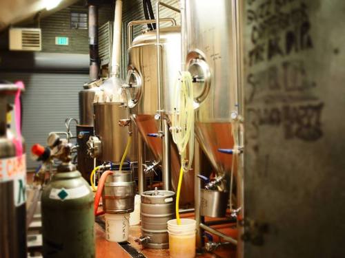 A brewery interior featuring stainless steel fermentation tanks and brewing equipment on a wooden counter.