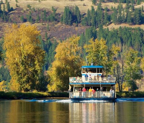 A scenic riverboat with passengers cruising on a calm river, surrounded by autumn-colored trees and hills.