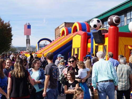 A lively outdoor event with a large inflatable slide and a crowd of people enjoying the festivities.